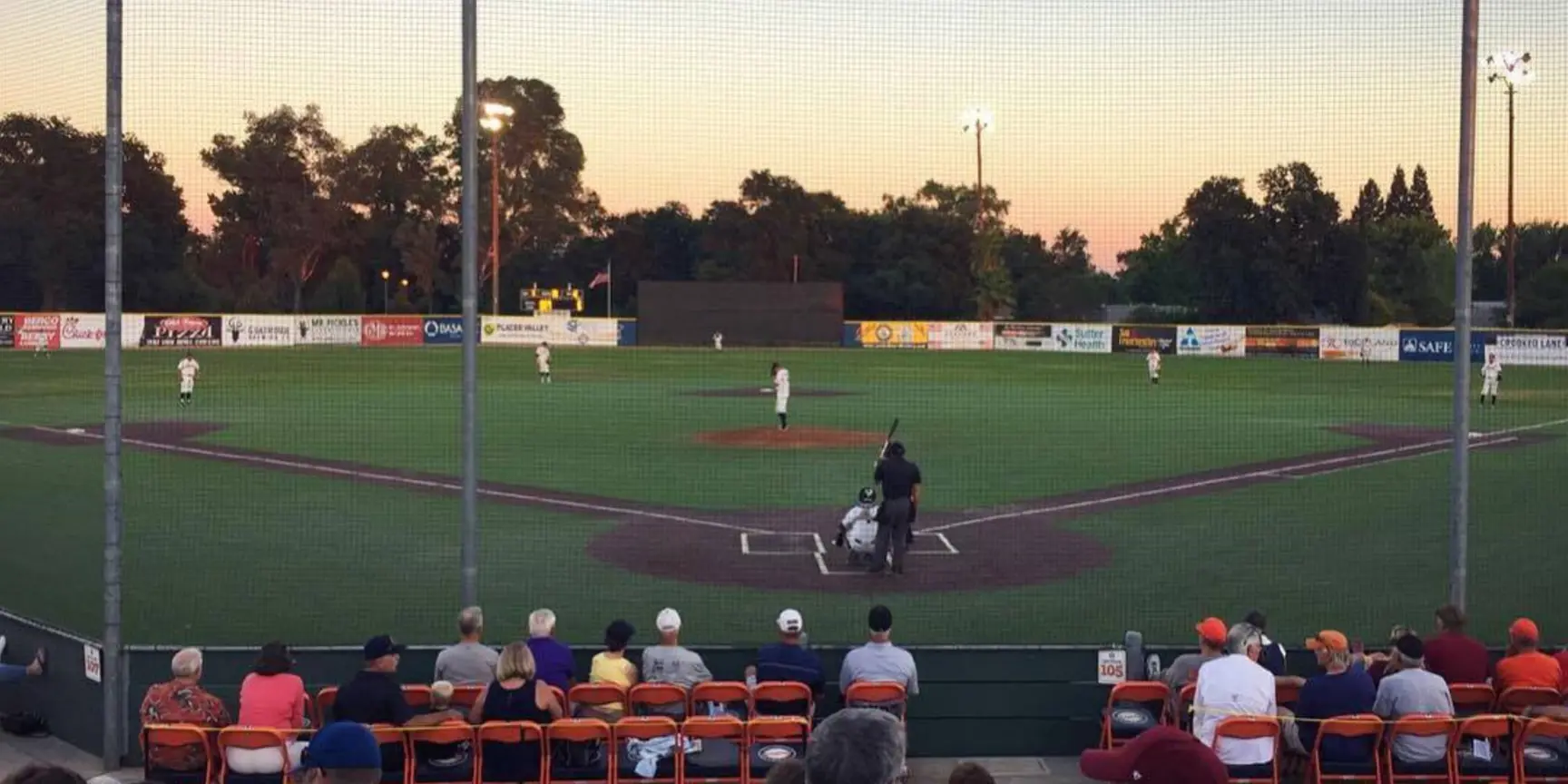 "Green baseball field with sunset in background"