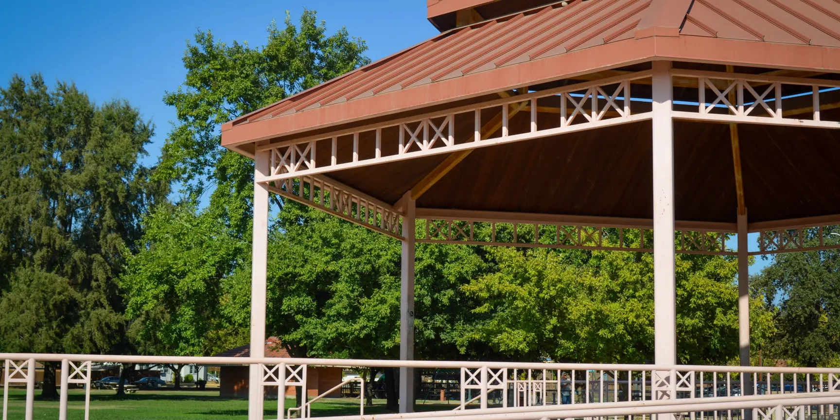 "Red shade structure with blue skies and green trees"