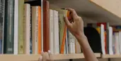 alt="hand picking a book from a bookshelf"