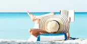 A woman in a sun hat reading on a beach