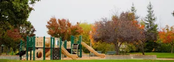 alt="Green playground with trees turning color in Autumn"