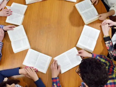 An overhead shot of a group of teens with books open on a table